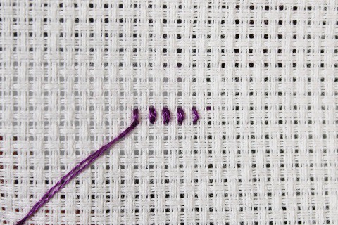 a short row of cross stitches viewed from the back done in purple embroidery floss on white aida