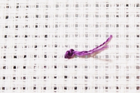 a knot tied on purple embroidery floss on white aid cloth