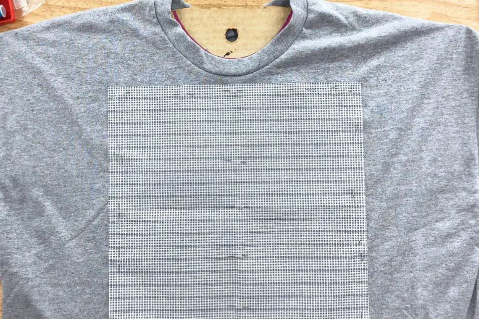 Waste Canvas pinned on a gray t-shirt.